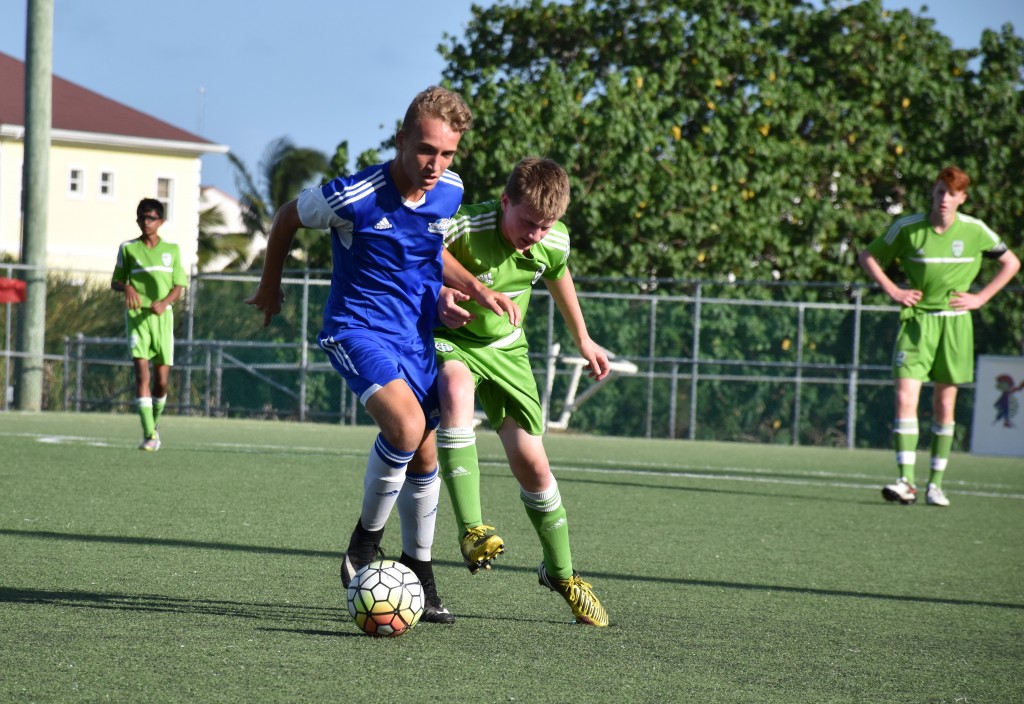 Academy's Jack Slater (blue) battles for possession against a REV player